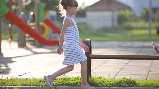 可悲的小女孩坐在幼儿园操场上的长椅上等妈妈 — 图库视频影像