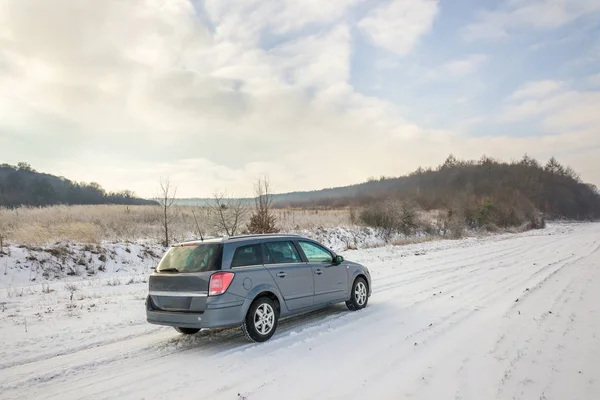 Family car driving on a dirt road in snow covered winter field.