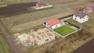 Biri ahşap çatı iskeleti ve diğeri de kırmızı kiremit çatılı iki özel evin yukarıdan aşağıya bakan görüntüsü..