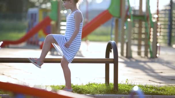 可爱的小女孩在幼儿园院子里的夏季操场上 坐在长椅上等妈妈 — 图库视频影像