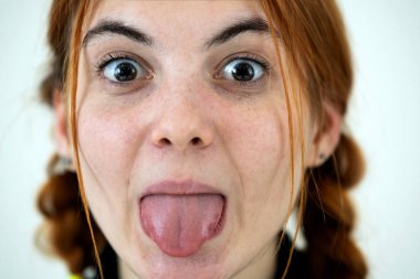 Closeup portrait of a funny redhead teenage girl with childish hairstyle sticking out her tongue isolated on white backround. clipart