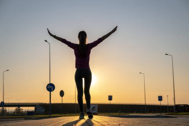 Gün batımında boş bir otoparkta duran genç bir kadının karanlık silueti..