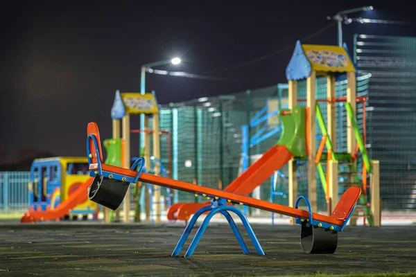 Seesaw swing in preschool yard with soft rubber flooring at night.