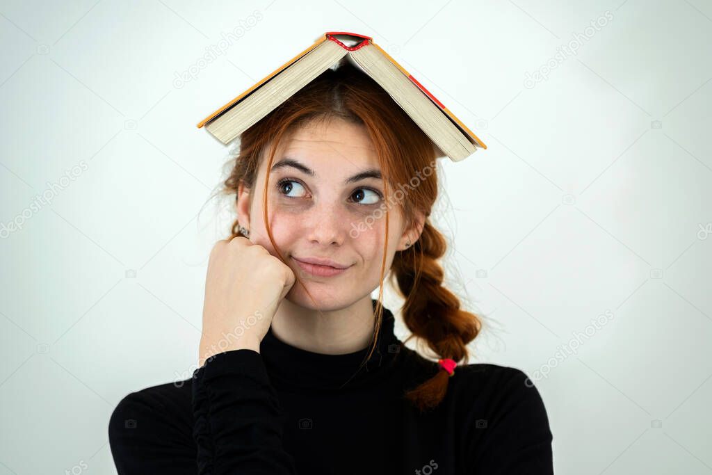 Portrait of funny young smiling student girl with an open book on her head. Reading and education concept.