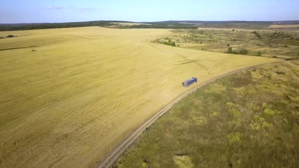 Vue aérienne d'un camion conduisant sur un chemin de terre entre des champs labourés faisant beaucoup de poussière .