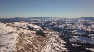 Kışın karla kaplı tepelerde dağınık evleri ve Ukrayna 'daki çıplak karanlık Karpat dağları olan küçük bir köyün havadan görünüşü..