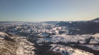 Kışın karla kaplı tepelerde dağınık evleri ve Ukrayna 'daki çıplak karanlık Karpat dağları olan küçük bir köyün havadan görünüşü..