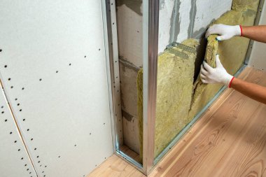 Bir oda duvarını mineral kaya yünü termal yalıtımı ile yalıtan işçiler.