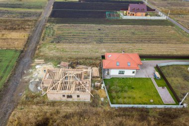 Biri ahşap çatı iskeleti ve diğeri de kırmızı kiremit çatılı iki özel evin yukarıdan aşağıya bakan görüntüsü..