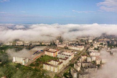 Yazın yeşil tarlalar arasında sıralı binalar ve kıvrımlı sokaklar olan bir kasaba ya da köyün üstündeki beyaz bulutların hava görüntüsü. Yukarıdan kırsal alan.