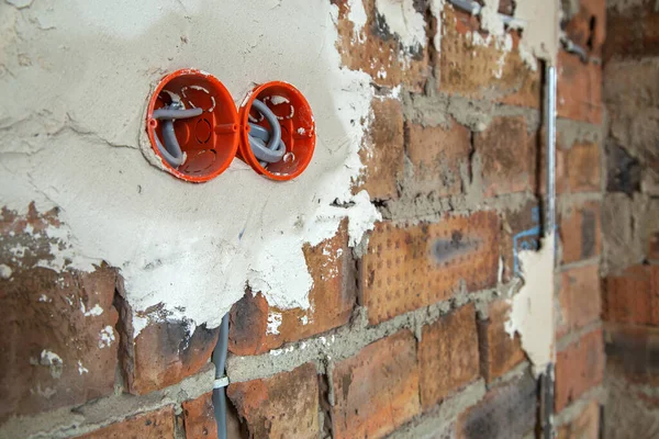 壁にワイヤー付きのソケットオレンジボックス レンガの壁に電気ソケット穴から突き出た電線の敷設 — ストック写真