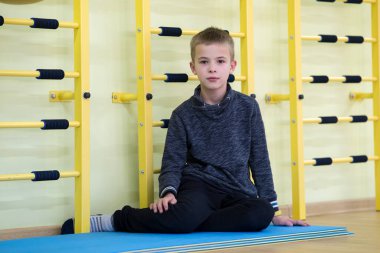 Genç çocuk antrenmandan sonra spor salonunun içinde yerde oturup rahatlıyor..