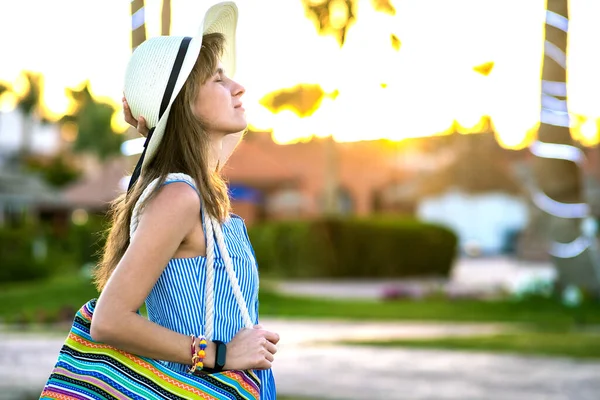 薄い青の夏のドレスと黄色のわら帽子を身に着けている若い女性は 外に立ってファッショナブルなショルダーバッグを保持夏の公園で暖かい天気を楽しんで日没 — ストック写真