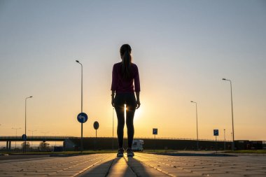 Gün batımında boş bir otoparkta duran genç bir kadının karanlık silueti..