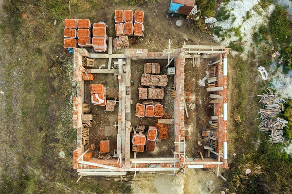 Aerial view of building site for future brick house, concrete foundation floor and stacks of yellow clay bricks for construction.