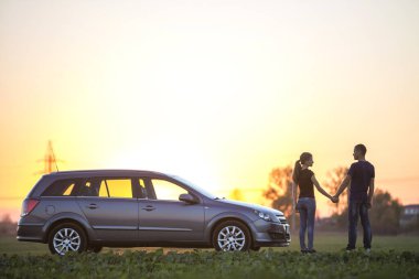 Genç çift, uzun at kuyruğu ve yakışıklı adam, yeşil alanında açık gökyüzü günbatımı veya gündoğumu kopya alan arka plan, gümüş renkli araba ayakta ince çekici kadın.