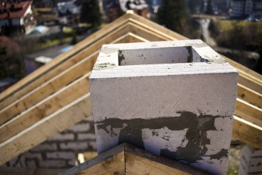 Kaba ahşap kirişlerden oluşan çatı iskeletinin ve bulanık yeşil arka planda köpük yalıtım bloklarından yapılmış bacanın yakın plan detayları. İnşaat, çatı, inşaat ve yenileme konsepti.