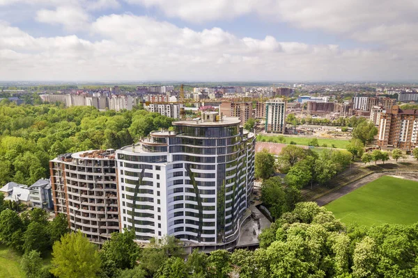 Apartment or office tall building unfinished under construction among green tree tops. Tower cranes on bright blue sky copy space background.