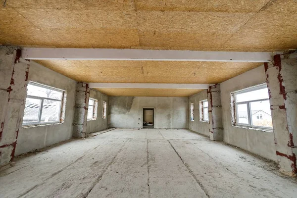 Unfinished apartment or house big loft room under reconstruction. Plywood ceiling, plastered walls, window openings, cement floor. Construction and renovation concept.