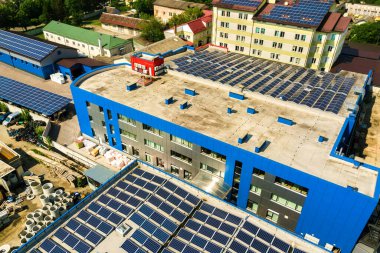 Sanayi binasının çatısına monte edilmiş birçok voltaik güneş panelinin hava görüntüsü.