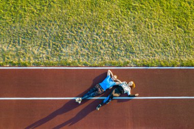 Yazın koşu maratonu yaptıktan sonra kırmızı kauçuk pistinde uzanan iki genç sporcu ve sporcunun hava manzarası..