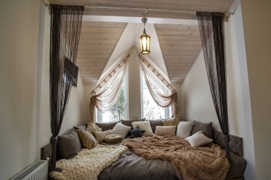 Modern bir evin içi geniş bir koridor ve büyük yumuşak bir dinlenme yeri. Çağdaş geniş kanepe, çok yastıklı ve pencereli ahşap tavan..