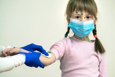 Doktor elleri, çocuğun elini dezenfeksiyona hazırlıyor mavi koruyucu maske takıyor suçiçeği, kızamık, kızamık ya da kızamık virüsü bulaşmış vücudunda isilikler var..