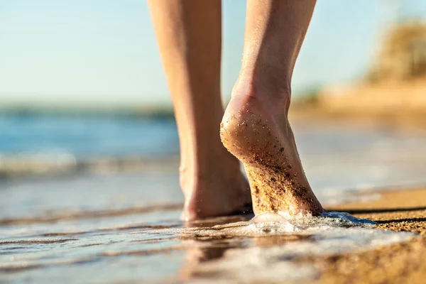 Close up of woman feet walking barefoot on sand beach in sea water. Vacation, travel and freedom concept. People relaxing in summer.