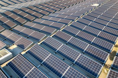 Sanayi binasının çatısına monte edilmiş birçok voltaik güneş panelinin hava görüntüsü.