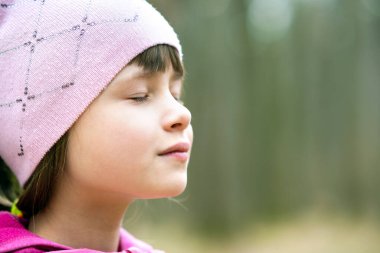 Pembe ceketli ve şapkalı güzel bir kızın portresi. Baharın erken saatlerinde açık havada güneşli bir günün tadını çıkarıyor..