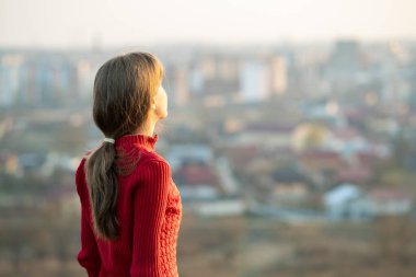 Kırmızı ceketli genç bayan dışarıda dikiliyor ve akşam manzarasının tadını çıkarıyor. Rahatlama, özgürlük ve sağIık kavramı.