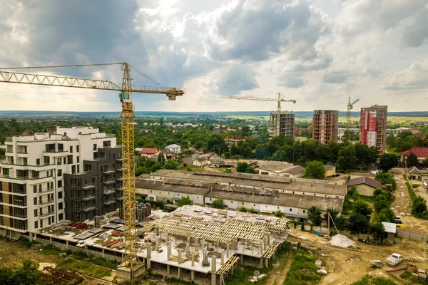 Aerial view of tower lifting crane and concrete frame of tall apartment residential building under construction in a city. Urban development and real estate growth concept.