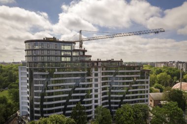 Daire veya ofis uzun boylu bina yeşil ağaç tops arasında inşaat altında tamamlanmamış. Parlak mavi gökyüzü kopya alanı arka planda kule vinçler.