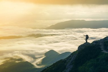 Geniş dağ panorama. Turist ile sırt çantası ile beyaz bulutlar kaplı vadi üzerinden kaldırdı elleriyle kayalık dağ yamacında küçük silüeti. Güzellik, Doğa, turizm ve seyahat kavramı
