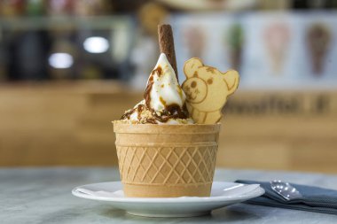 Dondurma Tatlı gofret fincan çikolatalı kurabiye ve yaratıcı dekorasyon Tepesi bulanık renkli iç arka plan üzerinde beyaz plaka.