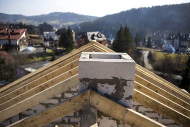 Kaba ahşap kirişlerden oluşan çatı iskeletinin ve bulanık yeşil arka planda köpük yalıtım bloklarından yapılmış bacanın yakın plan detayları. İnşaat, çatı, inşaat ve yenileme konsepti.