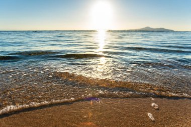 Yazın güneşli sahillerde, sarı kumsal üzerinde açık mavi suyla küçük deniz dalgalarını kapatın..
