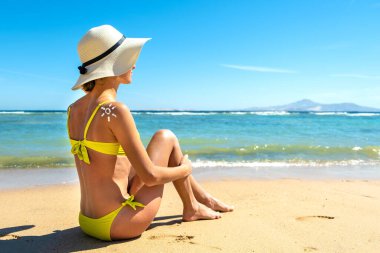 Omzunda güneş kremi ile plajda bronzlaşan genç bir kadının arka görüntüsü. UV güneş yanığı koruması ve güneş kremi konsepti