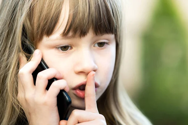 머리에 손가락으로 입술을 휴대폰으로 말하는 소녀의 스마트폰으로 의사소통하는 아이입니다 자녀들의 — 스톡 사진