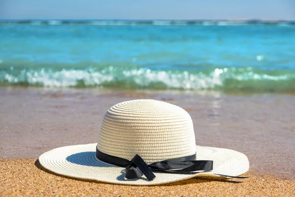White woman straw hat laying on tropical sand beach with blue vibrant ocean water in background on sunny summer day. Vacations and destination travel concept.