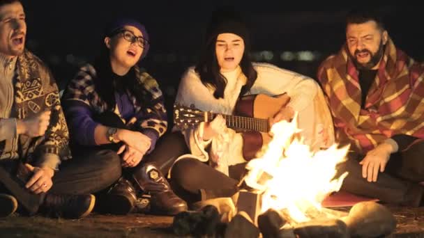 사람들 밖에서 모닥불 근처에 기타를 노래를 부르고 행복하게 이야기하는 즐긴다 — 비디오