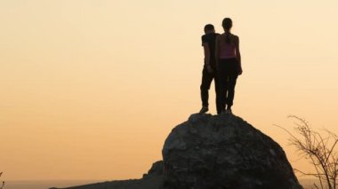 Erkek ve kadın yürüyüşçüler gün batımında dağlarda büyük kayalardan tırmanmak için birbirlerine yardım ederler. Akşam vakti yüksek kayalardan inen bir çift. Turizm, seyahat ve sağlıklı yaşam tarzı konsepti.