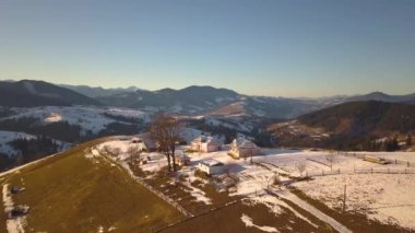 Kışın karla kaplı tepelerde dağınık evleri ve Ukrayna 'daki çıplak karanlık Karpat dağları olan küçük bir köyün havadan görünüşü..