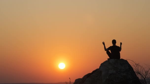 一个徒步旅行者在日落时分独自坐在大石头上的轮廓 男性游客在黄昏的自然中欣赏高山岩石的美景 旅游业 旅游和健康生活方式概念 — 图库视频影像