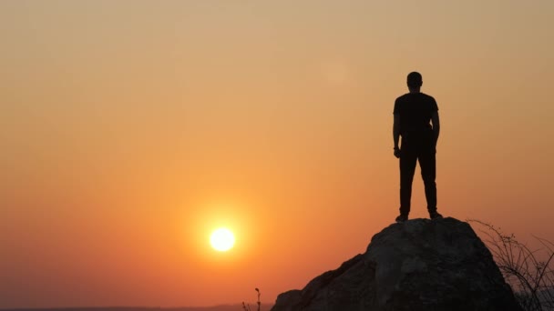 一个徒步旅行者在落日落山时独自跳上大石头的轮廓 傍晚时分 男性游客将双手高举在高高的岩石上 旅游业 旅游和健康生活方式概念 — 图库视频影像