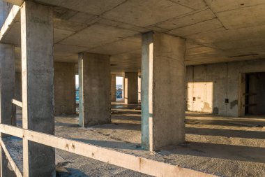 Bitmemiş çıplak duvarları ve inşaat halindeki gelecek duvarları destekleyen sütunları olan beton bir apartman dairesi..