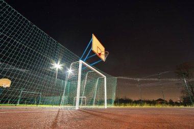 Açık havada top kapısı ve sepetli mini futbol ve basketbol sahası gece spot lambalarıyla aydınlatılmış yüksek korumalı çitlerle çevrili..
