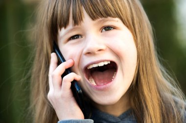 Cep telefonuyla konuşan uzun saçlı güzel bir kızın portresi. Küçük kız çocuk akıllı telefon kullanarak iletişim kuruyor. Çocuk iletişim konsepti.