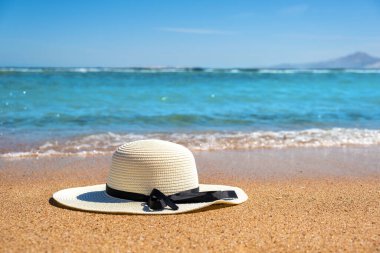 Beyaz kadın hasır şapka, güneşli yaz günlerinde tropikal kumsalda mavi canlı okyanus suyuyla yatıyordu. Tatiller ve yolculuk konsepti.