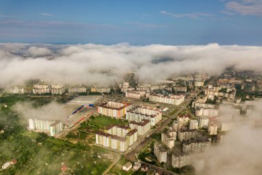 Yazın yeşil tarlalar arasında sıralı binalar ve kıvrımlı sokaklar olan bir kasaba ya da köyün üstündeki beyaz bulutların hava görüntüsü. Yukarıdan kırsal alan.